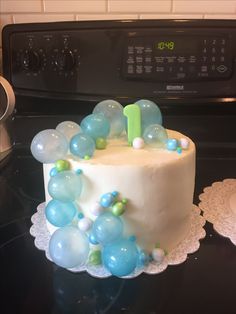 a white cake with blue and green balloons on it sitting on top of a stove