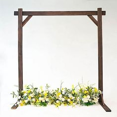 a wooden frame with flowers and greenery on the bottom is against a white wall