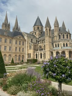 a large building with many towers and windows next to a flower garden in front of it