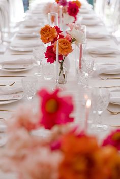 the table is set with white plates and pink flowers in vases on each side