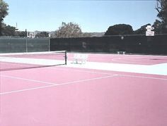 an empty tennis court with two white chairs on the sidelines and trees in the background