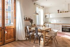 a table and chairs in a room with wooden floors, windows, and white walls