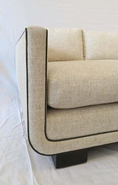 a beige couch with black legs on a white sheeted floor and wall behind it