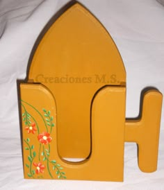 a yellow wooden toy house with flowers painted on the front and sides, sitting on a white sheet