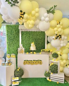 a lemon themed baby shower with balloons and greenery on the wall, cake table