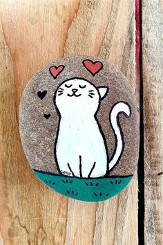 a painted rock with a white cat on it's face and hearts in the background