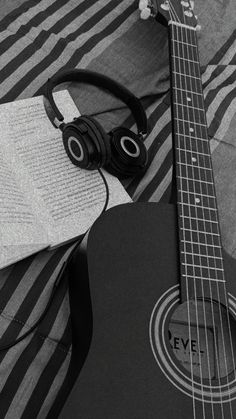 an acoustic guitar and headphones are laying on a striped blanket with a notepad