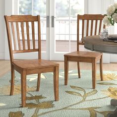 two wooden chairs sitting on top of a rug in front of a dining room table