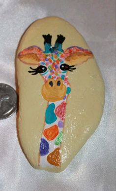 a painted rock with a giraffe's face on it next to a coin