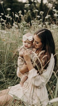 a woman holding a baby in her arms while sitting on the ground surrounded by tall grass