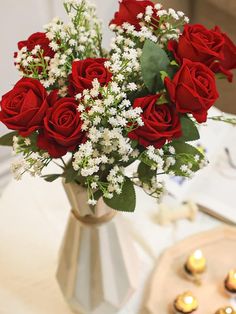 a vase filled with red roses on top of a table next to candles and plates