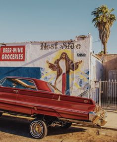 an old red car parked in front of a building with a painted mural on it