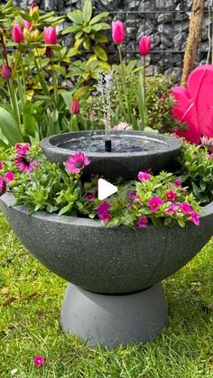 an outdoor fountain with flowers in it and water coming out of the top, surrounded by pink tulips