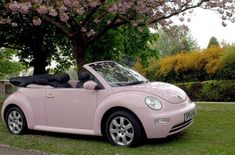 a pink convertible car parked in front of a tree