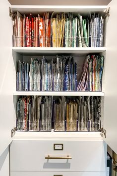 an open book shelf filled with lots of books on top of white drawers and gold handles