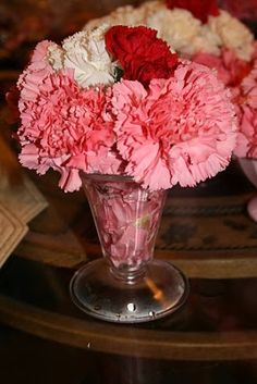 pink and white carnations in a glass vase on a table with other flowers