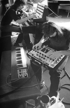 two people sitting in front of an electronic keyboard and sound equipment, one playing the piano