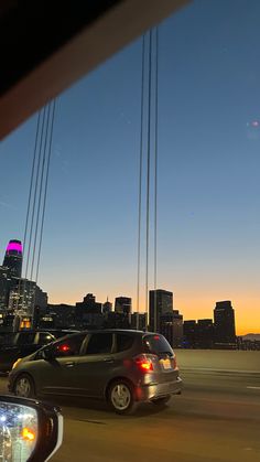 two cars driving on the road in front of a cityscape at sunset or dawn