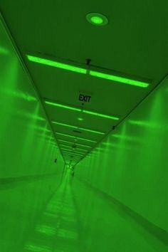 an exit sign is lit up in the middle of a long hallway with green walls