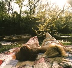 two women laying on a plaid blanket in the woods, one with her back to the camera