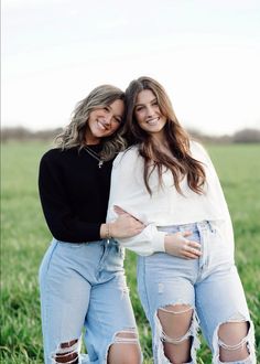 two young women standing next to each other in a field with their arms around each other