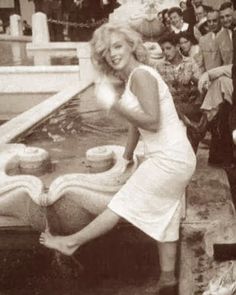 a woman in a white dress leaning over a fountain