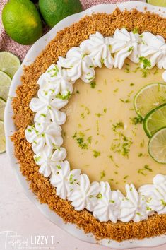 a key lime pie on a white plate with limes around it and two lime wedges