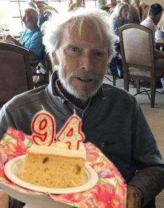 an older man holding a cake with the number 94 on it in front of him