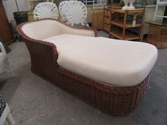 a wicker chaise lounge with white cushions in a room filled with other furniture