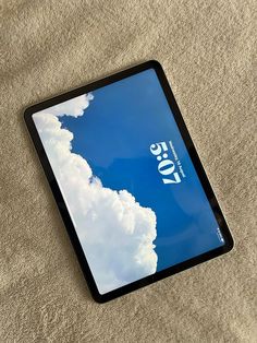 an ipad with the cover pulled down on a bed sheet that has clouds in the sky