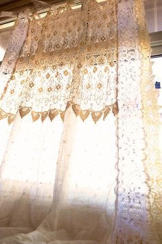 an open window with white curtains and laces on the curtain valance in front of it