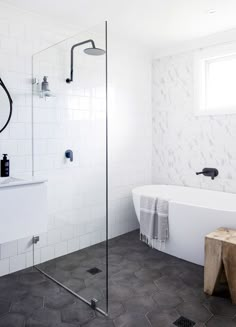 a bathroom with a white bathtub, black and white tile flooring and a wooden stool