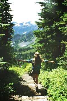 a woman is walking up a trail in the mountains with her arms outstretched and hands out