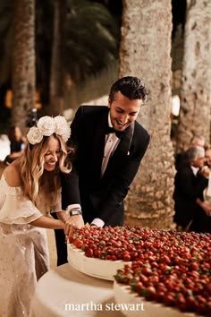 a man and woman cutting into a cake with strawberries on it in front of people