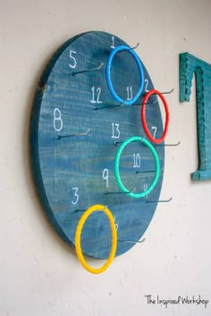 a blue clock with numbers and rings on the wall next to a pair of scissors