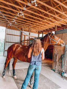 a woman standing next to a brown horse in a barn