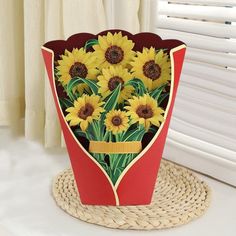 a bouquet of sunflowers in a red paper box on a wicker place mat