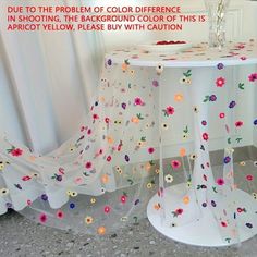 a white table with flowers on it next to a vase filled with water and a curtain