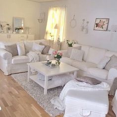 a living room filled with white furniture and flowers on top of a coffee table in front of a window