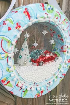 a christmas ornament hanging on a wooden fence with a red car in the snow