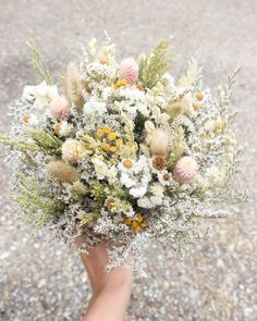 a bouquet of flowers in someone's hand on the ground with gravel and rocks