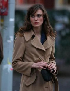 a woman is walking down the street with her hand in her pocket and wearing a trench coat