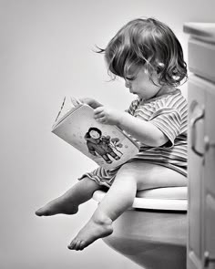 a young child sitting on top of a toilet reading a book with scissors drawn on it