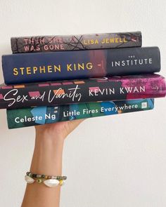 a stack of books held up by a woman's hand in front of a white wall