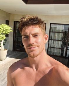 a shirtless man standing in front of a house next to a potted plant