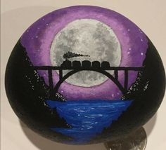 a painted rock sitting on top of a metal keychain with a bridge and moon in the background