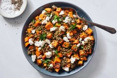 a bowl filled with lentils, carrots and feta cheese next to a spoon