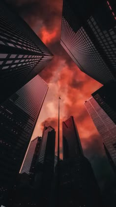 some very tall buildings with red clouds in the sky behind them and one light at the top