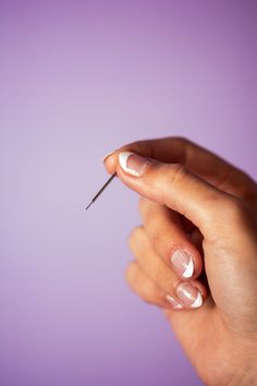 a woman's hand holding a tiny toothpick in front of a purple background