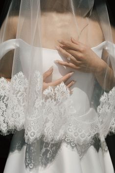 a woman wearing a wedding dress and veil with her hands on the back of her shoulder